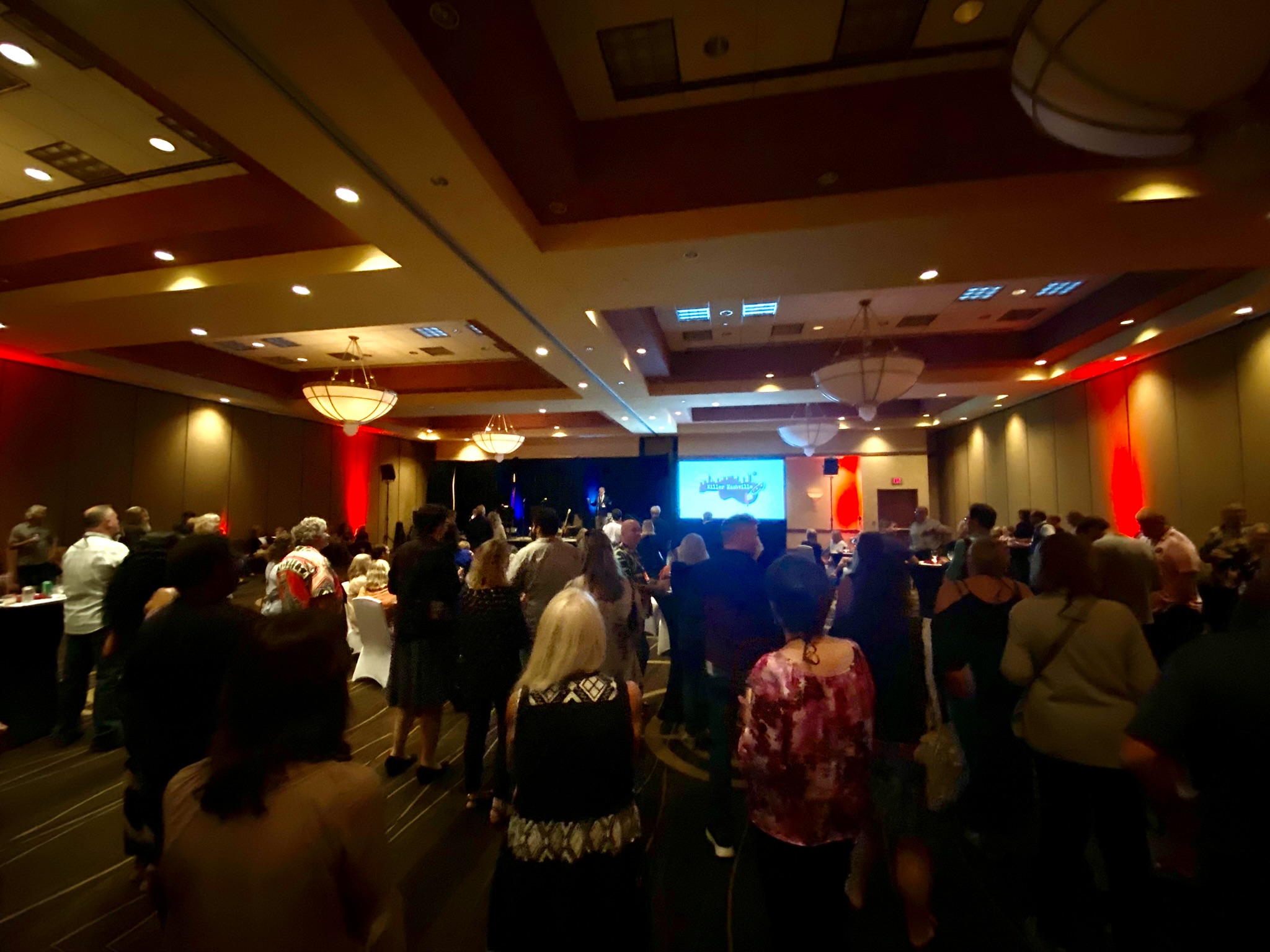 A darkened room full of people at a social event at Killer Nashville.